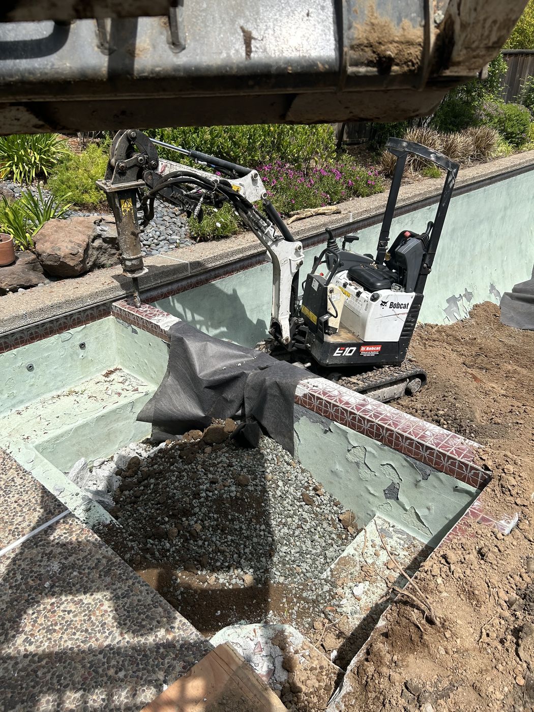 Mini excavator breaking down the top bond beam and coping of a pool