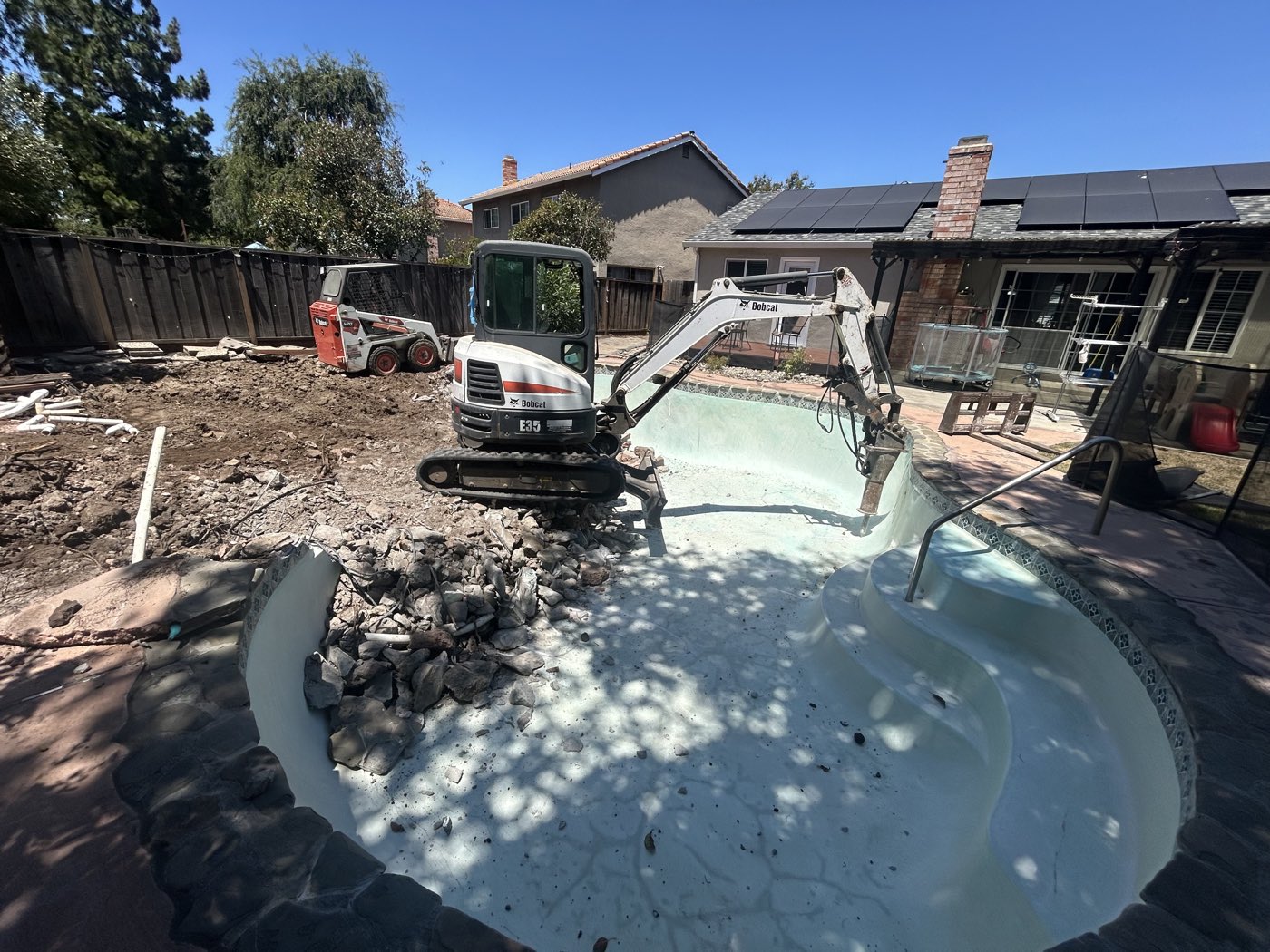Bobcat E35 excavator breaking into a pool shell for complete removal