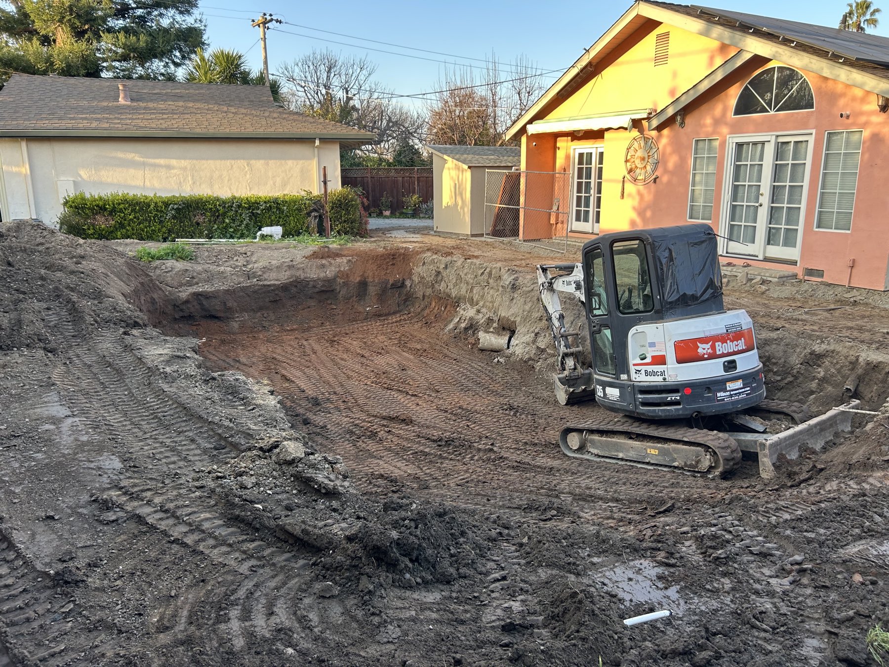Mini excavator positioned at the edge of a freshly excavated pool cavity