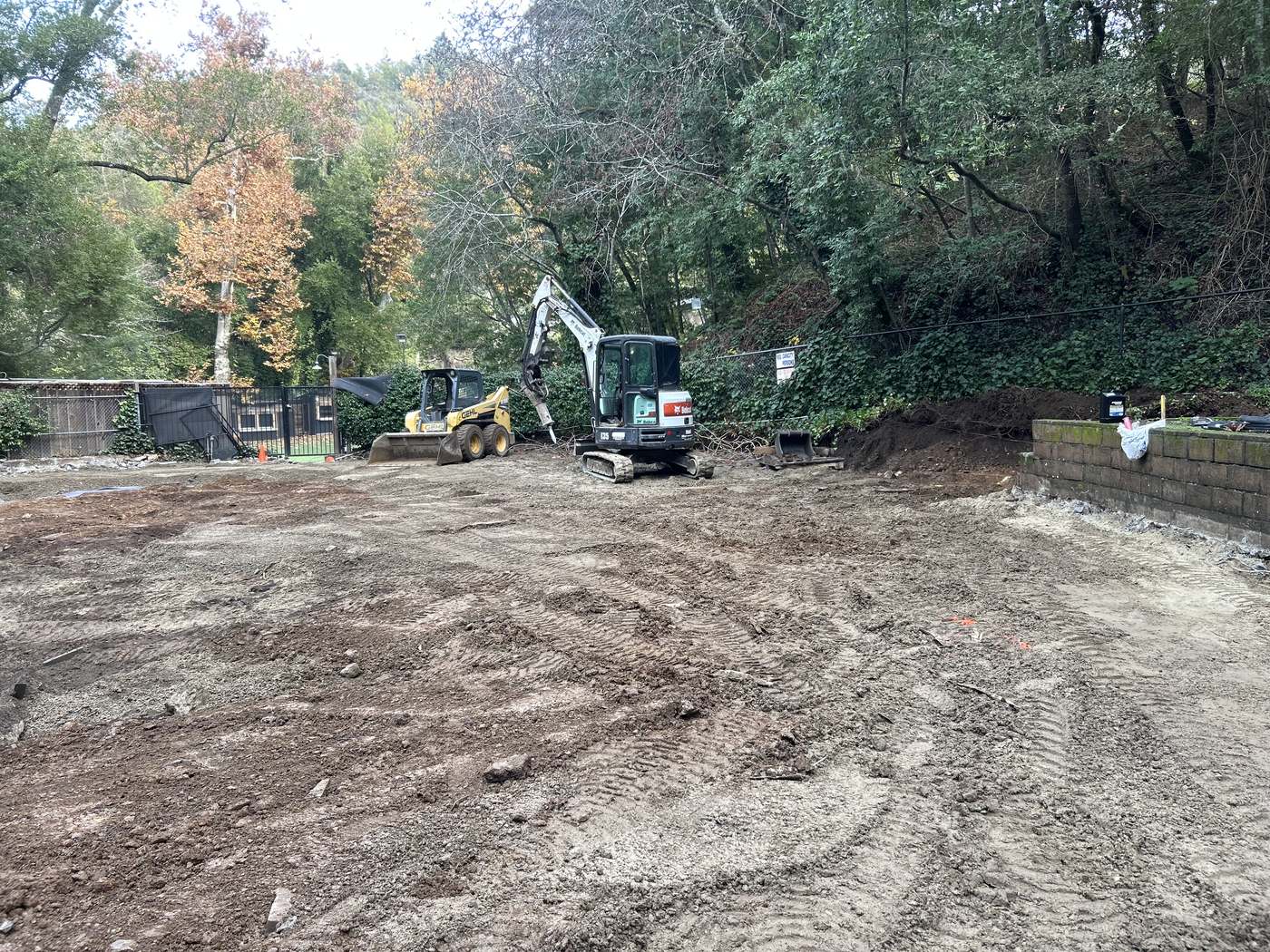 Excavator and skid steer clearing and grading a wooded hillside lot