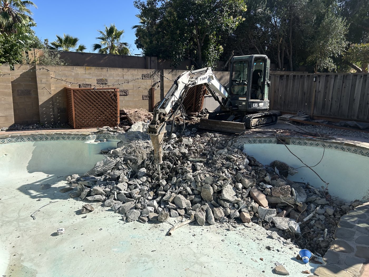 Excavator breaking up a swimming pool shell during partial removal