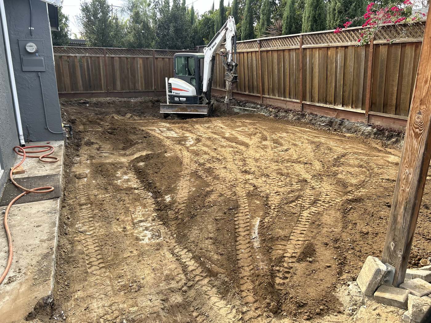 Mini excavator backfilling a pool footprint in a narrow, fenced side yard