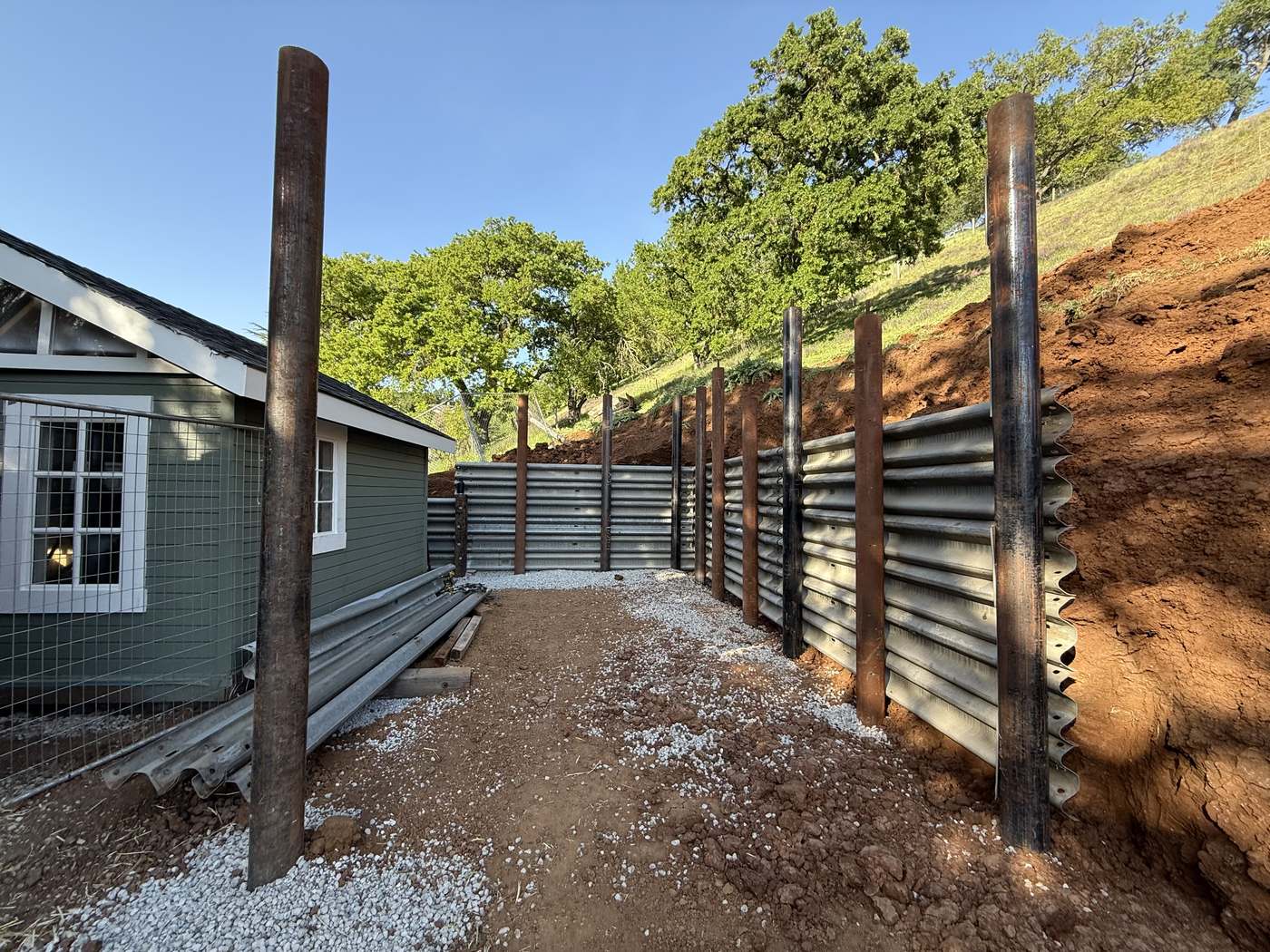 Steel I-beam posts set for a corrugated retaining wall on a hillside